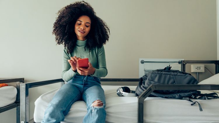 young female traveler on a hostel bunk using a smartphone